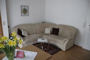 A living room with a beige sofa, a small white side table, a vase with yellow flowers, and a framed picture on the wall. - Kuckucksnest Vacation Rental: Enjoy the morning sun on the balcony. (Minheim)
