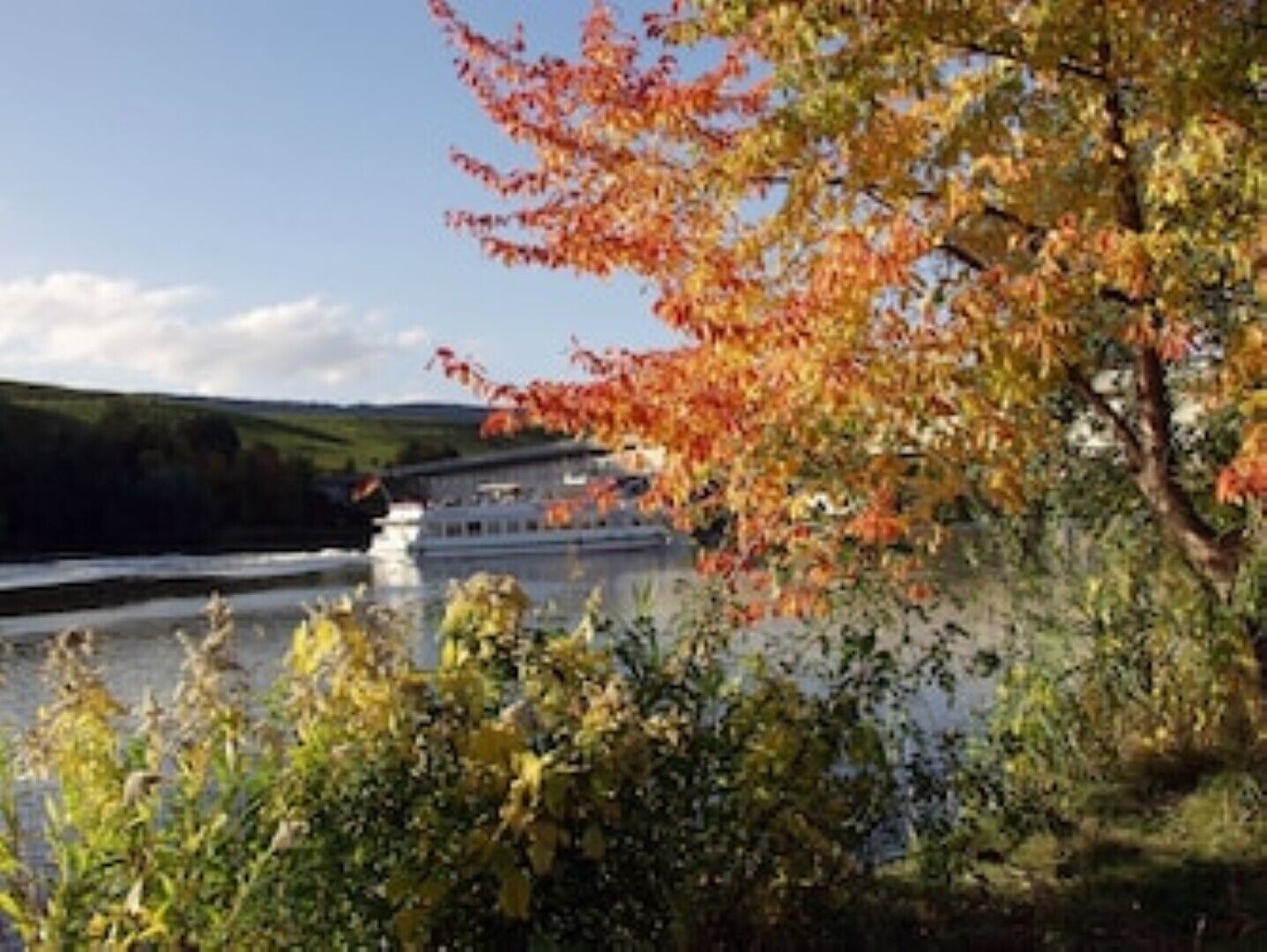 A river with a boat docked on the right, surrounded by autumn foliage.