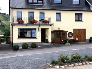 A two-story building with a balcony, a front door, and a small garden area with plants and flowers. - Kuckucksnest Vacation Rental: Enjoy the morning sun on the balcony. (Minheim)