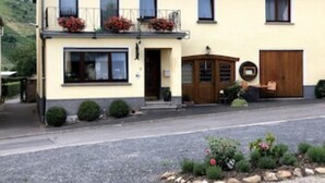 A two-story building with a balcony, a front door, and a small garden area with plants and flowers. - Apartment "Moselblick", A great view of the greenery and enjoy the evening sun (Minheim)