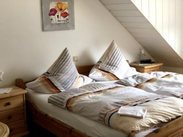 A bedroom with a sloped ceiling, a wooden bed frame, and a nightstand with a lamp.