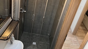 A modern bathroom with a glass-enclosed shower, a white sink, and a mirror with lights.