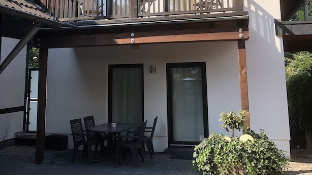 A two-story building with a balcony, a patio area with a table and chairs, and a small garden.