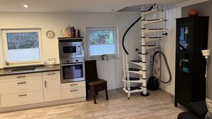 A compact kitchen with built-in appliances, a chair, a spiral staircase, and a sofa.