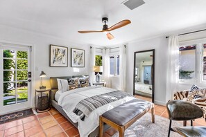 A bedroom with a bed, bedside tables, a ceiling fan, and a view of the outdoors.