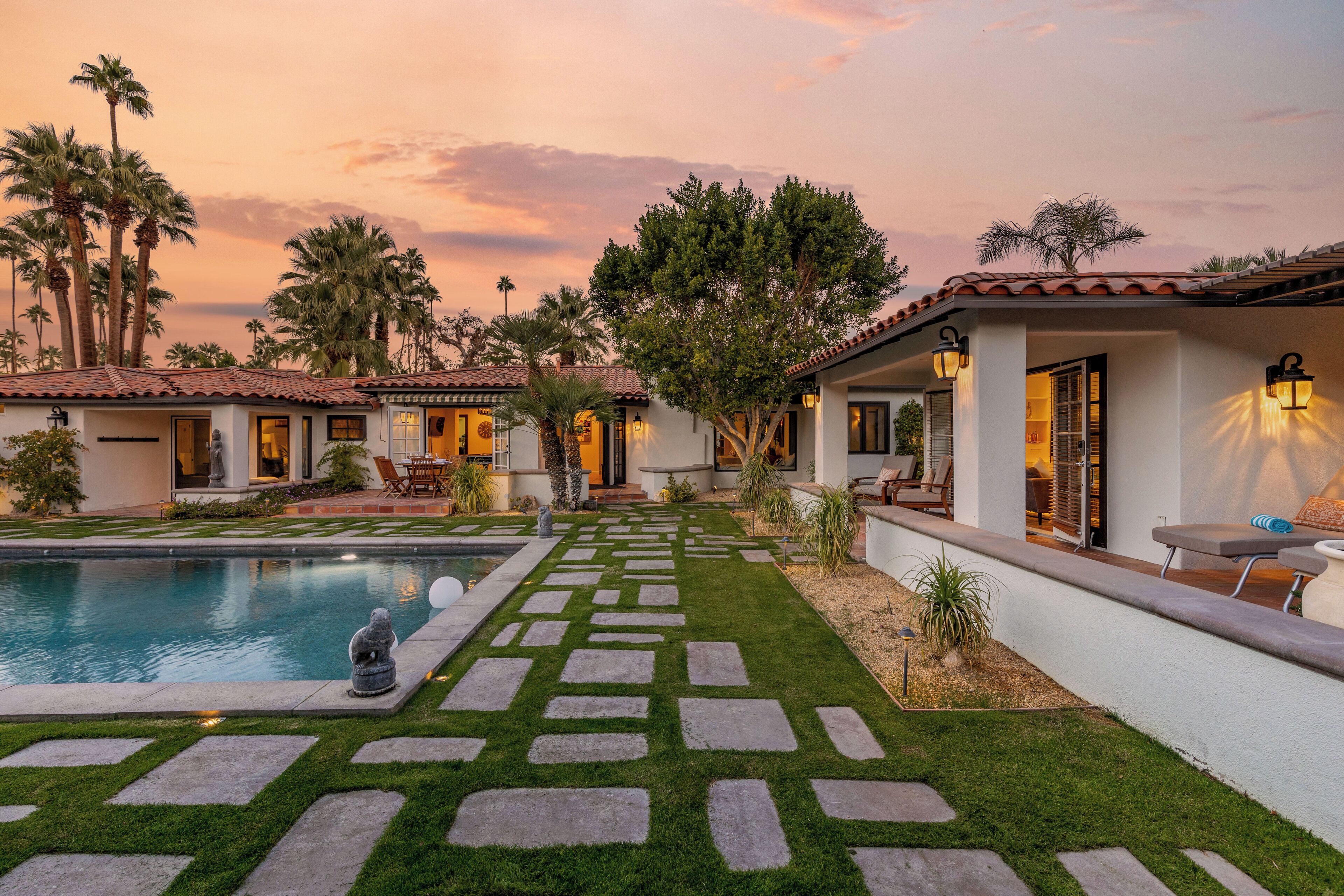 A pool with stone stepping stones leading to a patio area with outdoor furniture.