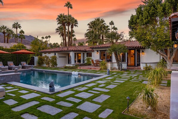 A pool with a stone border, palm trees, and a sunset sky.