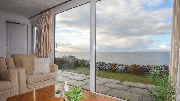 A living room with a large window overlooking a rocky coastline. - Bramble Bank (Harlech)