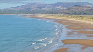 A coastal landscape with a sandy beach, gentle waves, and distant mountains under a clear sky. - Bramble Bank (Harlech)