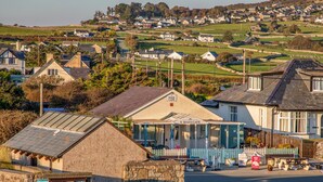 A coastal town with a cafe named "Y Maes Cafe" featuring stone buildings, a clear road, and a view of the village in the background. - Bramble Bank (Harlech)