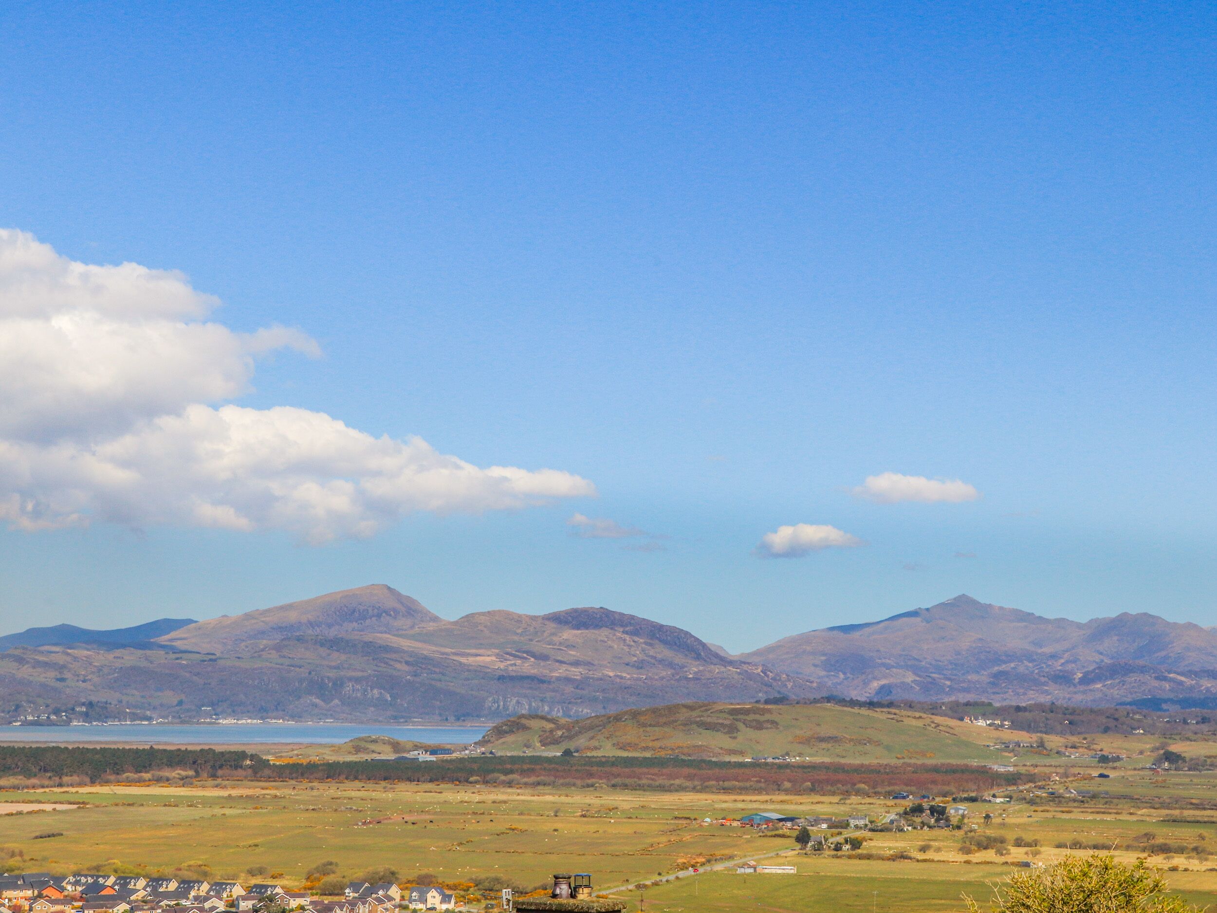 Une vue panoramique d’un paysage côtier comprenant des montagnes, une étendue d’eau et un village avec des maisons.