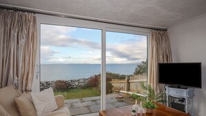 A living room with a large sliding glass door leading to a balcony with a view of the sea. - Bramble Bank (Harlech)