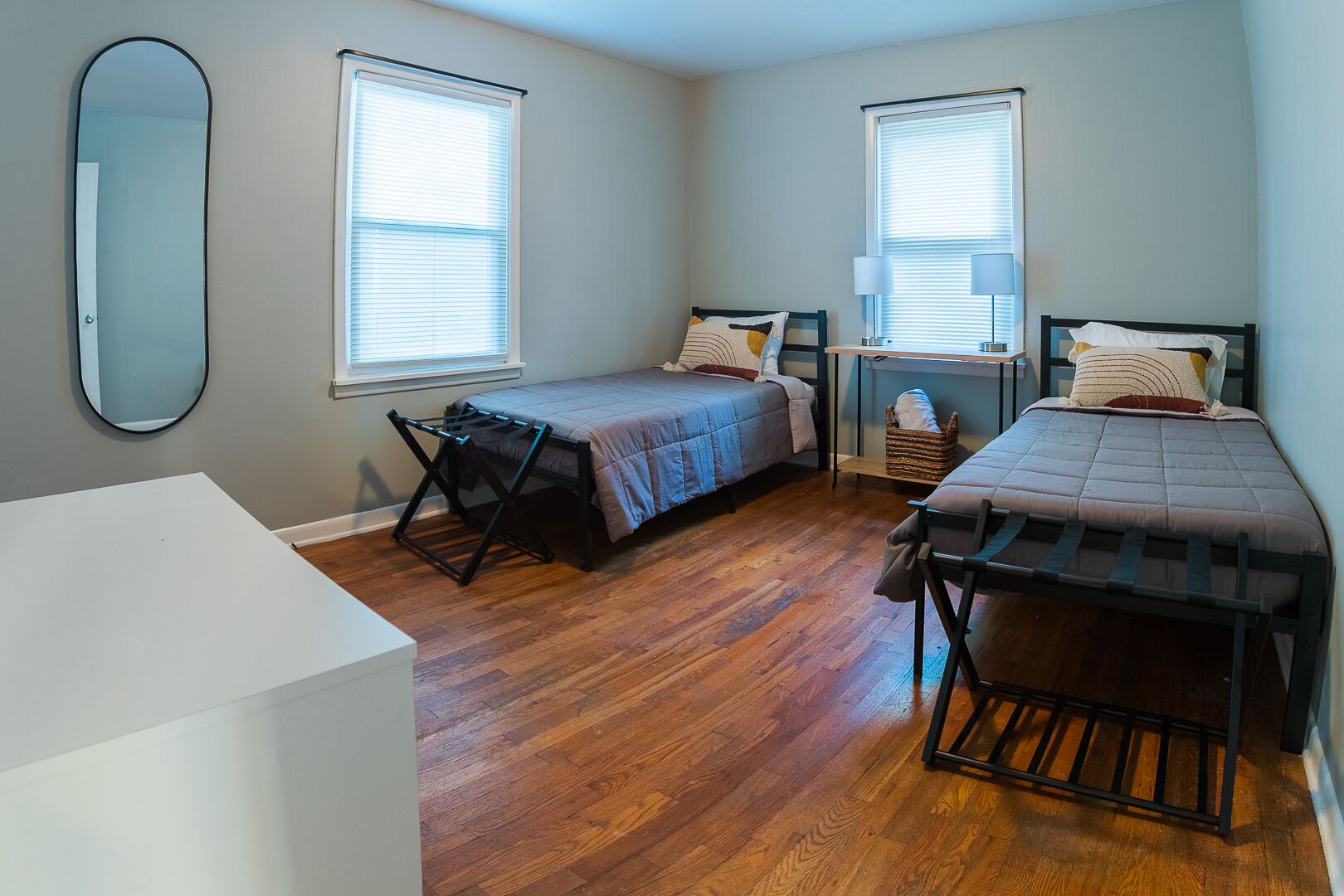 A small, well-lit bedroom with two beds, a desk, and a large mirror.
