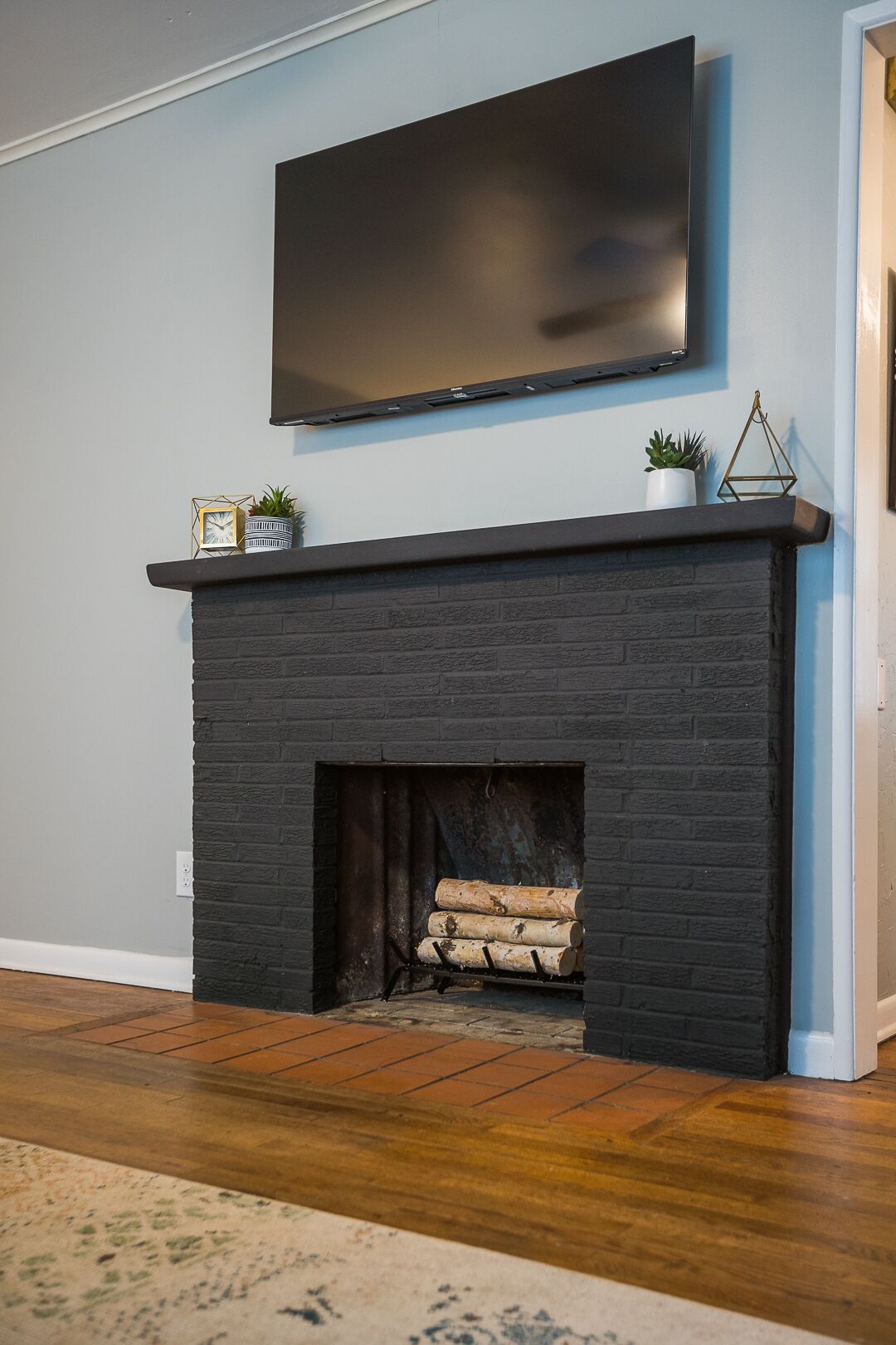 A modern living room with a black brick fireplace, a mounted flat-screen TV, and a small shelf with decorative items.