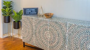A reception area with a wooden floor, a patterned console table, a round mirror, a welcome sign, and two potted plants. - The Robberson House close to Mercy, WOW, MSU (Springfield)