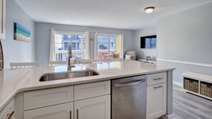 A modern kitchen with a large island, white cabinetry, and a stainless steel sink. - Sunskipper E2 - 2 bedroom ocean view condo (Carolina Beach)