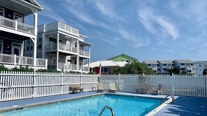 A swimming pool with a white fence and lounge chairs, surrounded by multi-story buildings with balconies. - Sunskipper E2 - 2 bedroom ocean view condo (Carolina Beach)