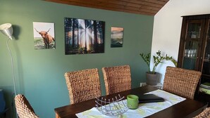 Un comedor con una mesa de madera, sillas de mimbre y una pared verde decorada con cuadros.