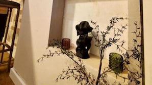 A corner of a room with a white wall, a wooden chair, a small black sculpture, and a decorative branch.