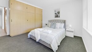 A bedroom with a large wooden wardrobe, a bed with a grey headboard, a nightstand, and a framed picture on the wall. - The Family Retreat - Near Mt Panorama & Racecourse (South Bathurst)