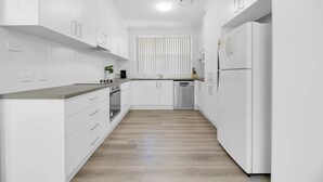 A modern kitchen with white cabinetry, a wooden floor, and a built-in dishwasher. - The Family Retreat - Near Mt Panorama & Racecourse (South Bathurst)