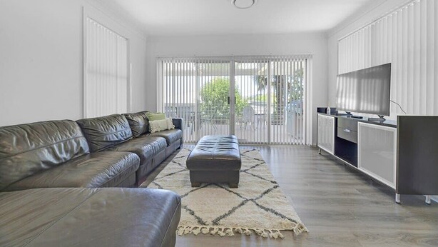 A modern living room with a leather sofa, a matching ottoman, and a TV on a cabinet. - The Family Retreat - Near Mt Panorama & Racecourse (South Bathurst)