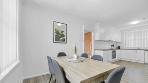 A modern kitchen with white cabinets, a wooden dining table, and a small plant on the table. - The Family Retreat - Near Mt Panorama & Racecourse (South Bathurst)