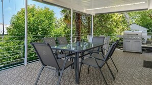 An outdoor patio with a glass-top table surrounded by chairs, a grill, and a view of greenery. - The Family Retreat - Near Mt Panorama & Racecourse (South Bathurst)