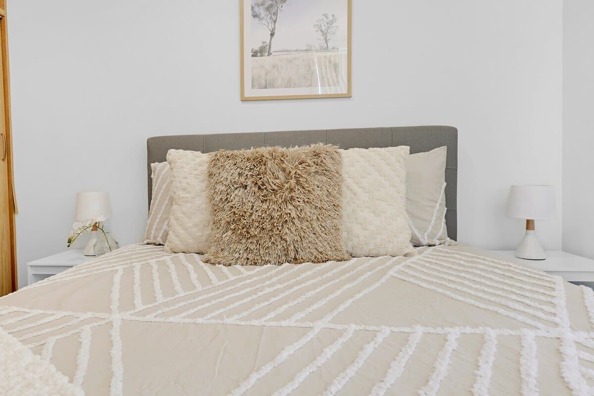Ein ordentlich eingerichtetes Schlafzimmer mit einem großen Bett, einem flauschigen Zierkissen und einem gerahmten Bild an der Wand.