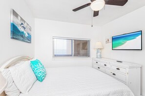 A bedroom with a bed, a ceiling fan, a window with blinds, a TV, and artwork on the walls. - Renovated 2B Gulf Front Condo @ Emerald Isle 805! (Pensacola Beach)