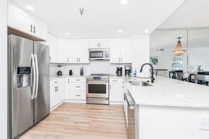 A modern kitchen with white cabinetry, stainless steel appliances, a central island, and a chandelier. - Renovated 2B Gulf Front Condo @ Emerald Isle 805! (Pensacola Beach)