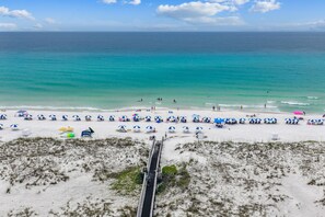A beach with a long pier leading to the shore, numerous beach umbrellas, and a clear view of the ocean. - Renovated 2B Gulf Front Condo @ Emerald Isle 805! (Pensacola Beach)