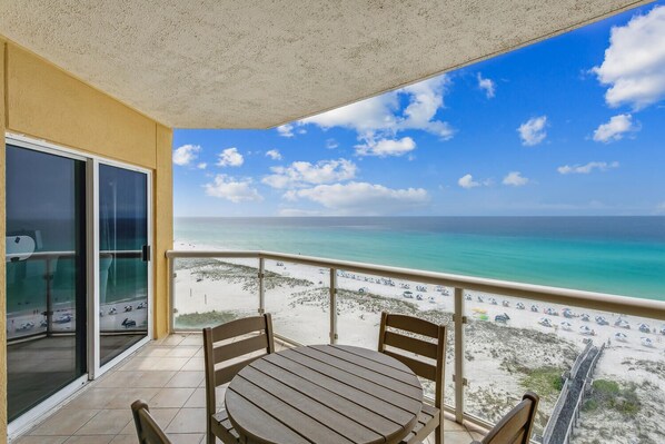 Ein Balkon mit Tisch und Stühlen, der Blick auf einen Strand mit klarem türkisblauem Wasser und einem sandigen Ufer bietet.
