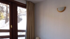 A bedroom with a bed, a window with curtains, a bedside table with a lamp, and a wall-mounted light fixture.