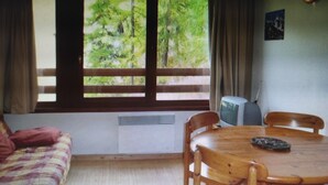 A room with a large window, a wooden table with chairs, a sofa, and a small television.