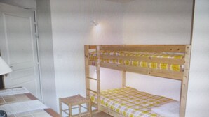 A room with a bunk bed, a small wooden stool, and a desk with a lamp.