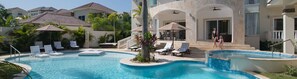 Una piscina con sillas de descanso y sombrillas, rodeada de edificios con balcones y ventanas.
