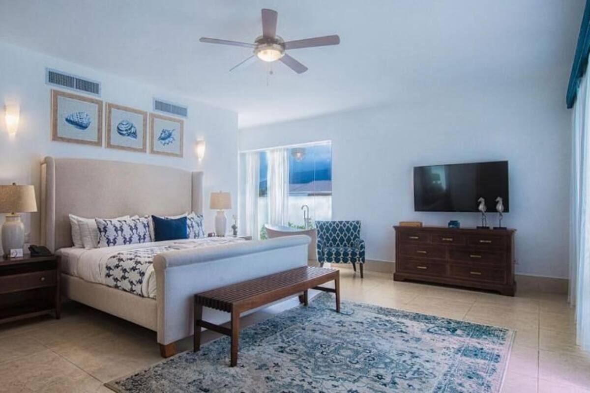 A bedroom with a bed, bedside tables, a bench, a TV, and a view of the outdoors.