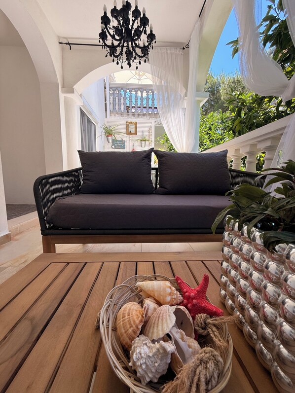 A balcony with a wicker sofa, a wooden table, and a basket of seashells.
