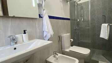 A modern bathroom with a sink, bidet, toilet, and glass-enclosed shower.