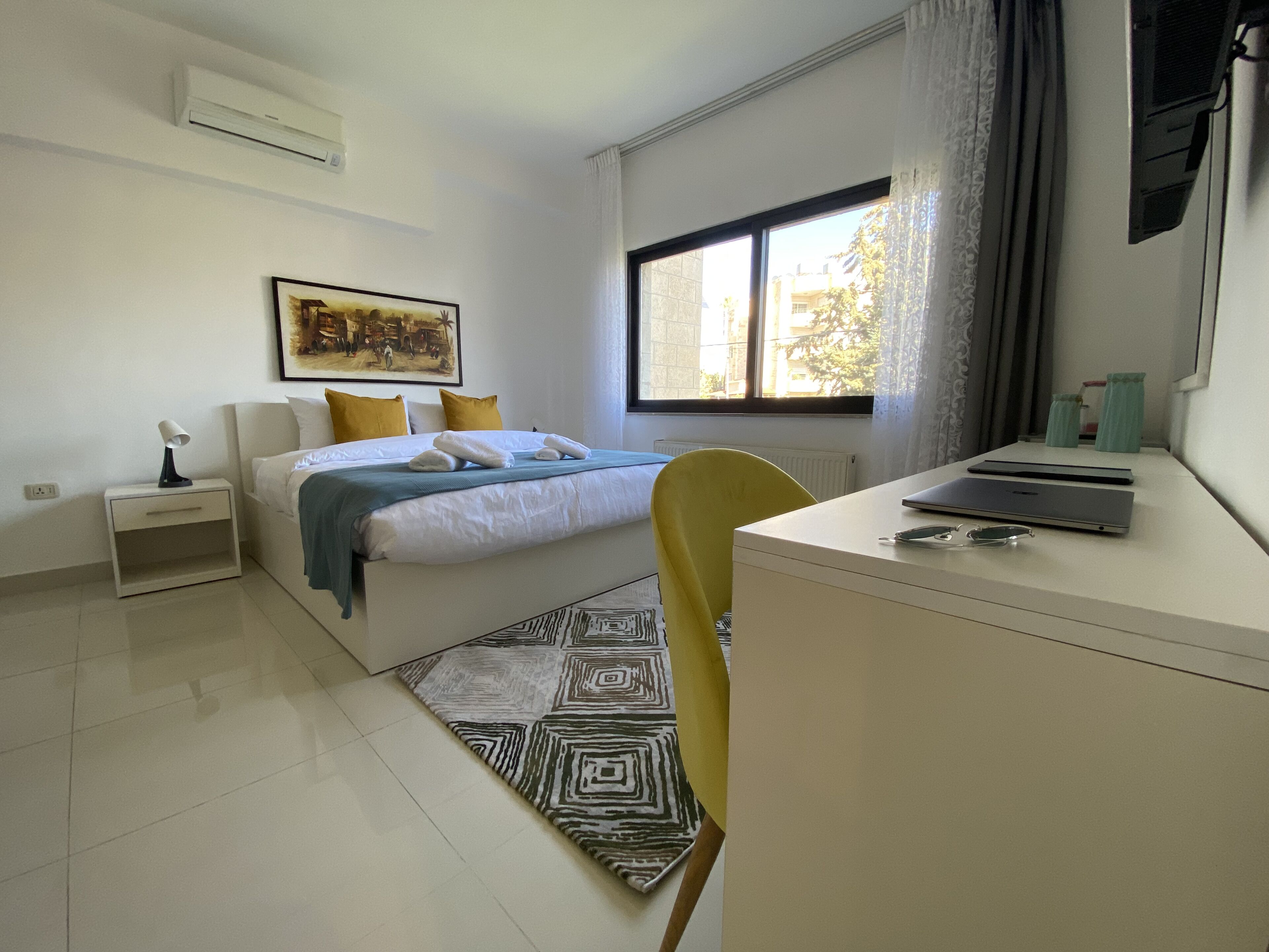 A modern bedroom with a bed, bedside table, and a desk with a laptop.
