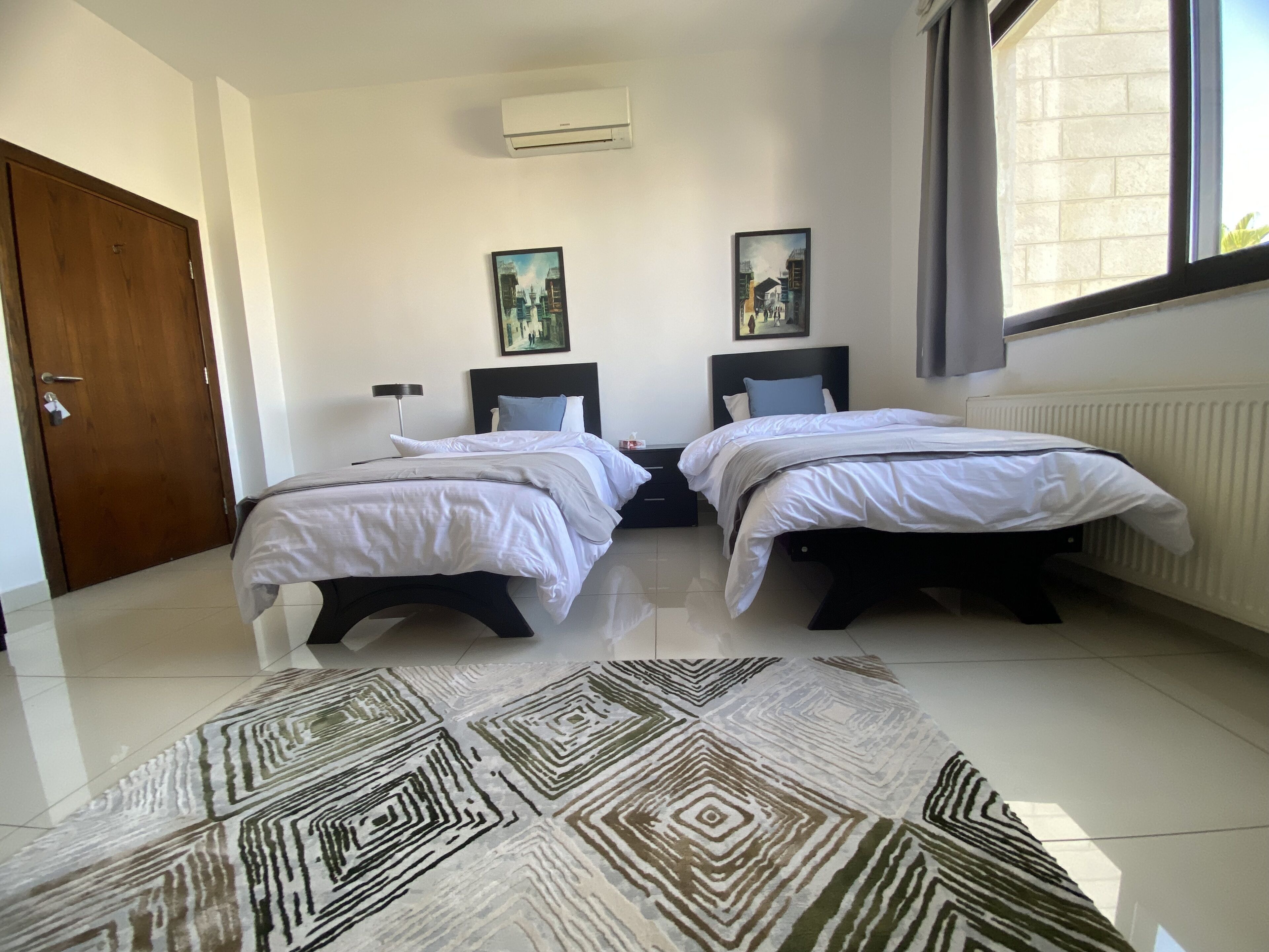 Una camera d'albergo moderna e pulita con due letti, un'ampia finestra e un tappeto decorato.