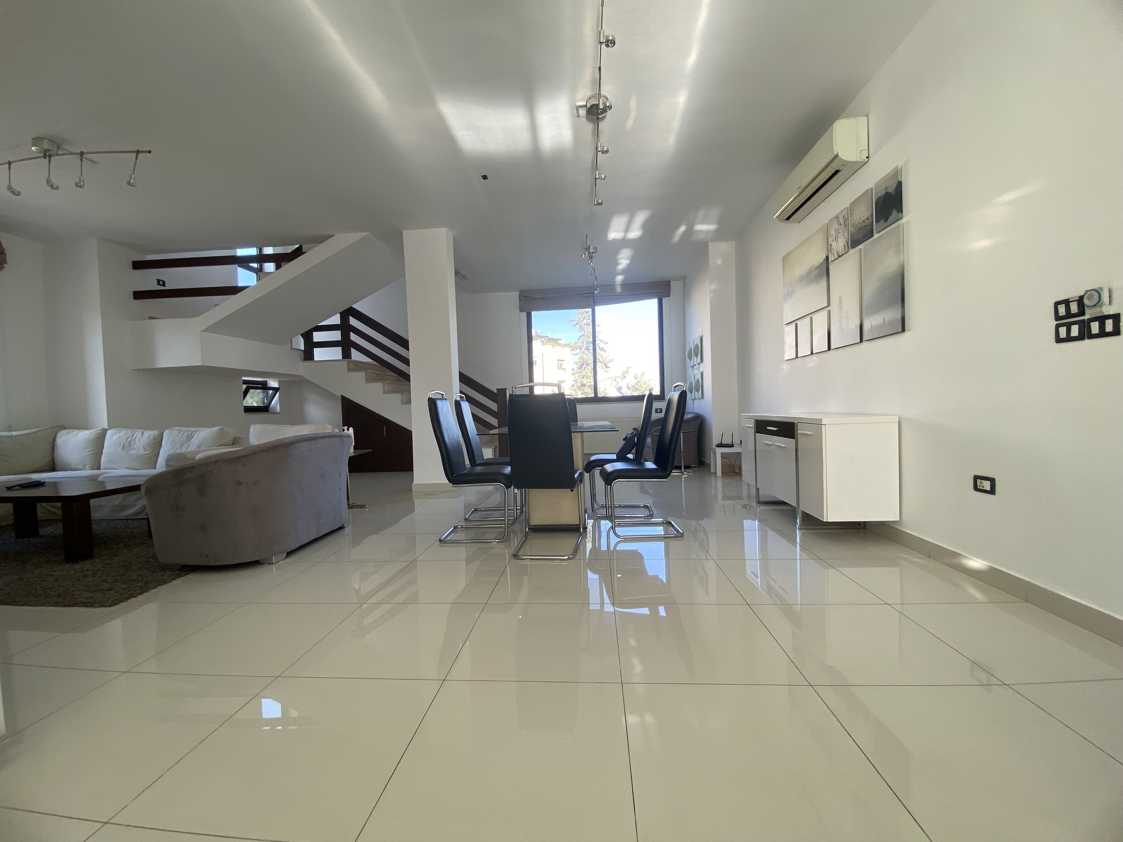 Una sala moderna con un sofá, sillas, una mesa de comedor y una escalera.