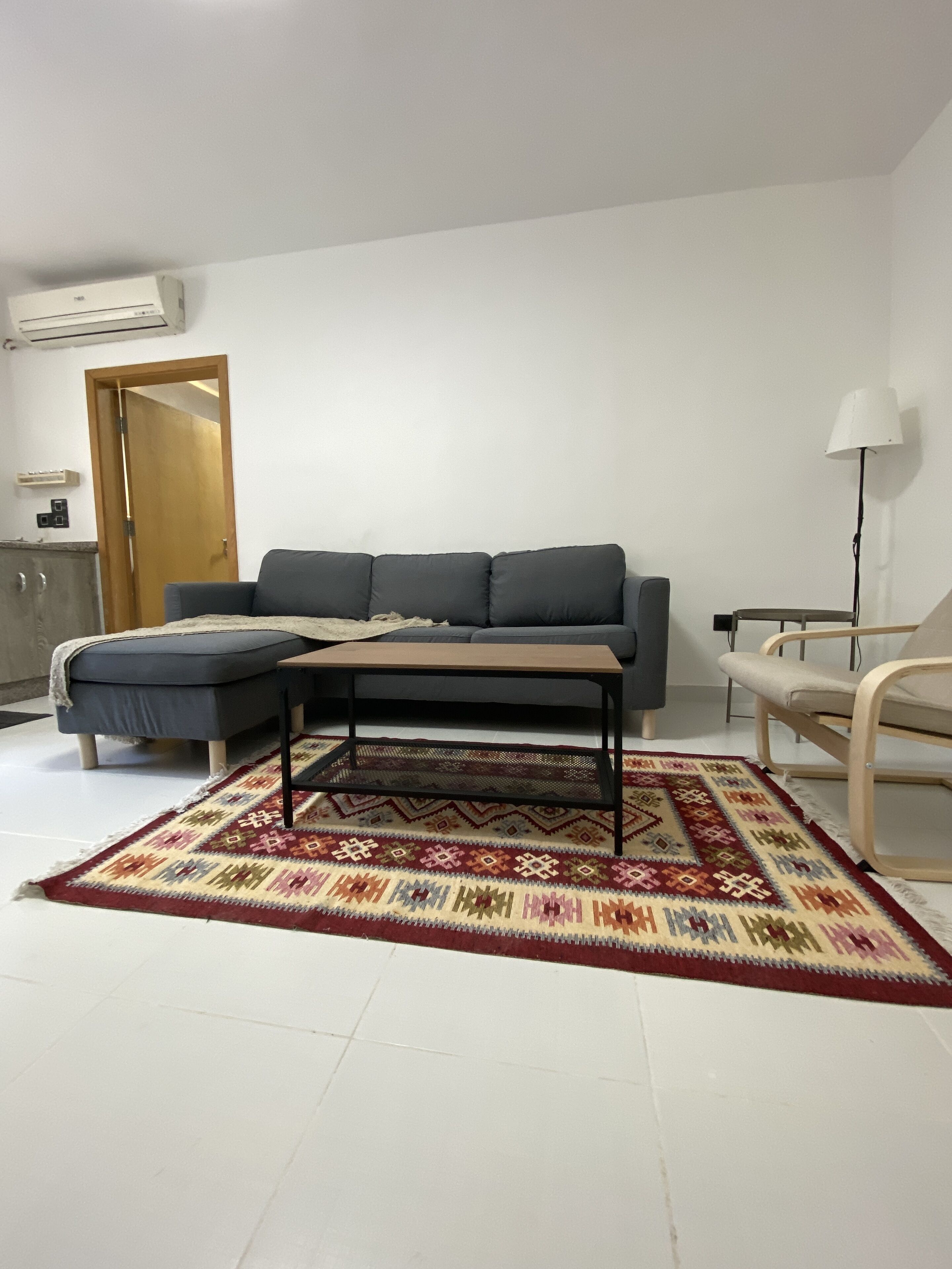 A living room with a grey sofa, a small wooden coffee table, a patterned rug, a wooden chair, and a lamp.