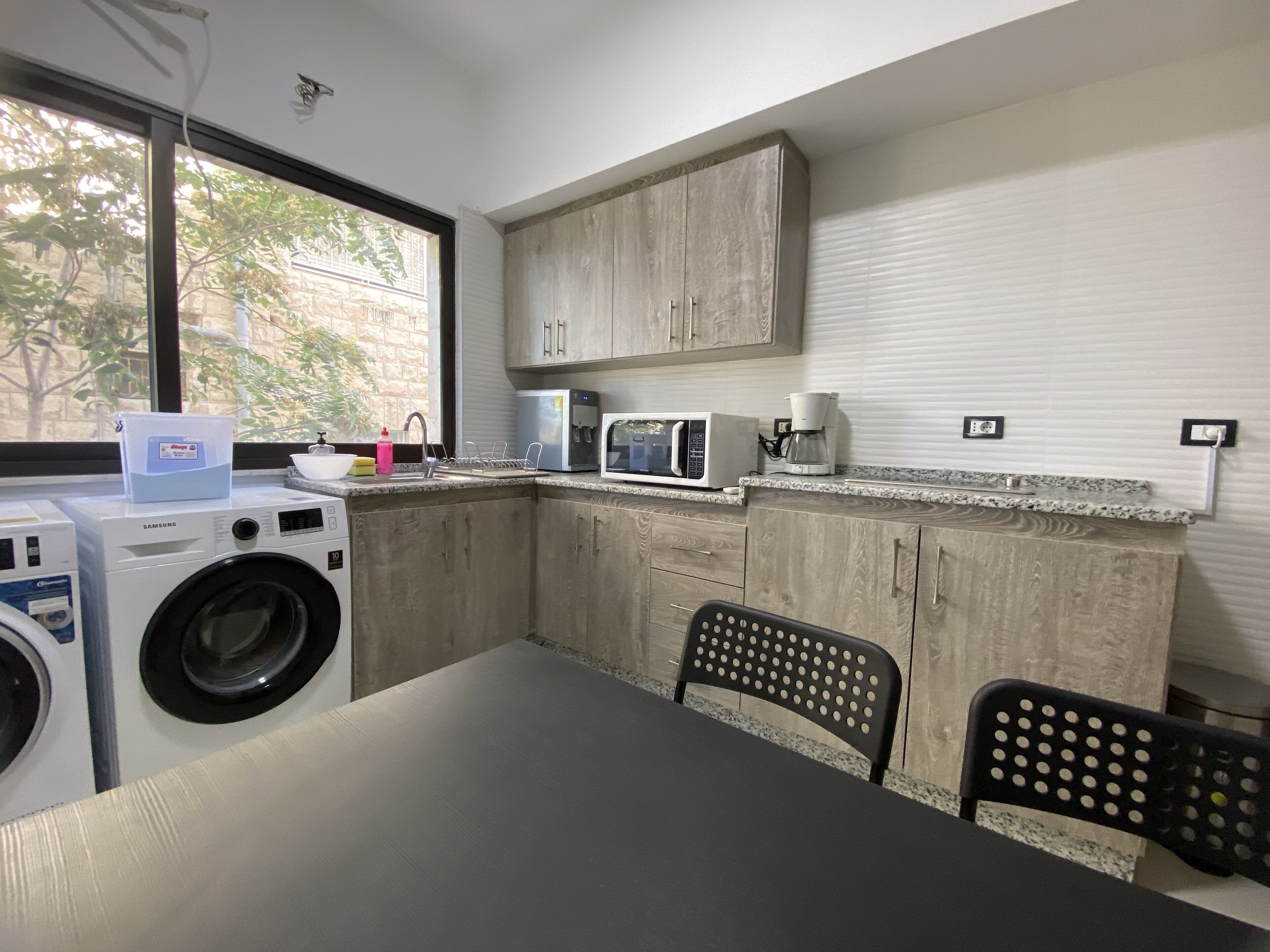 Cocina compacta con lavadora, microondas y cafetera. Una ventana ofrece luz natural y vistas al exterior.