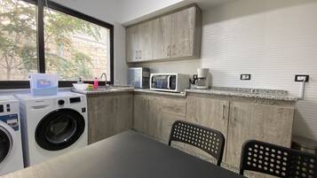 Cocina compacta con lavadora, microondas y cafetera. Una ventana ofrece luz natural y vistas al exterior.
