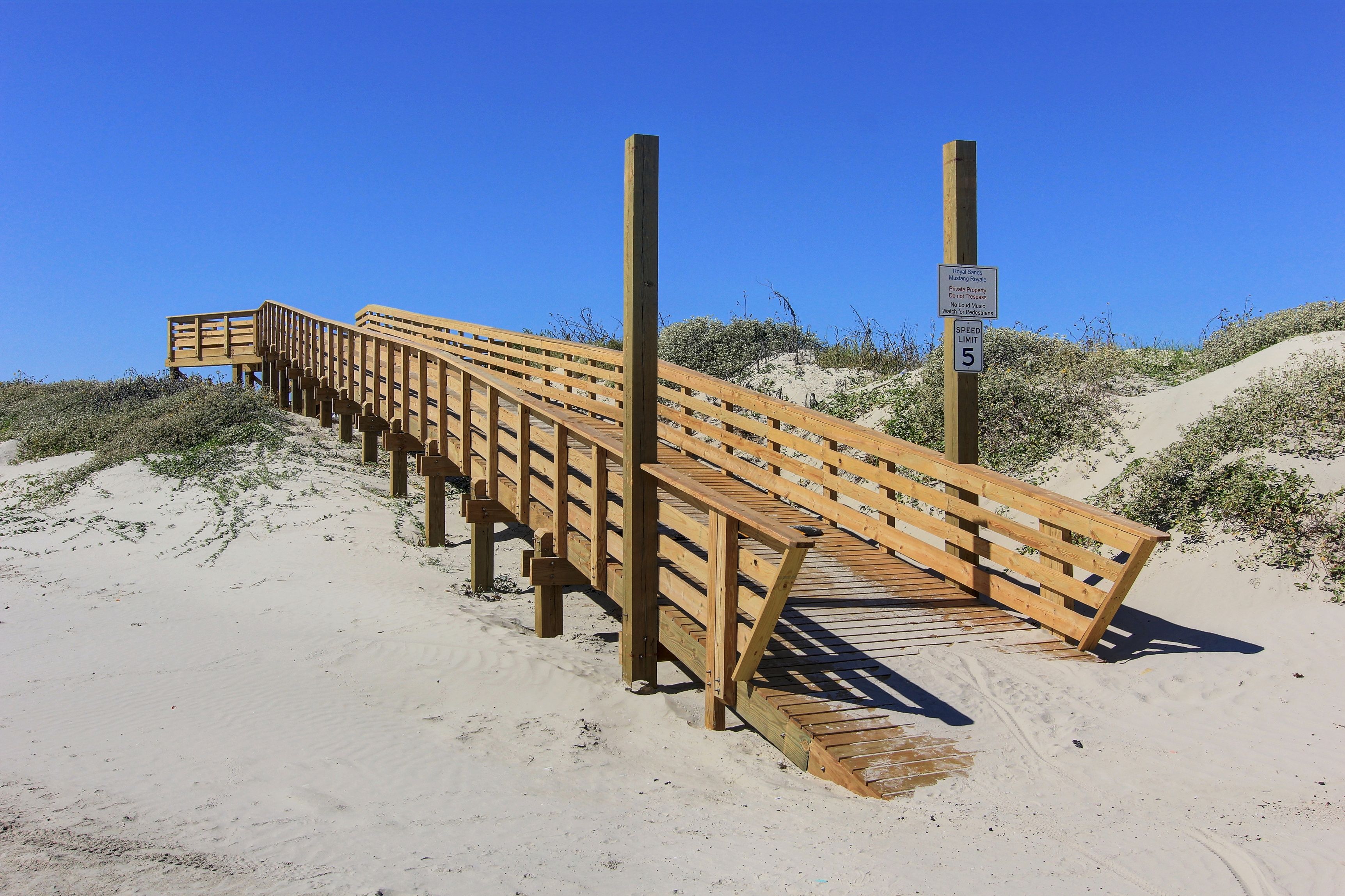 A wooden boardwalk leading to a wooden structure, surrounded by sand dunes.