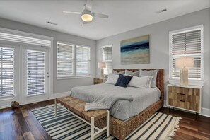 A bedroom with a large bed, a ceiling fan, and a view of the outdoors through the windows. - PINFISH! — Carolina Beach's Most Loved and Best Equipped Beach House (Carolina Beach)