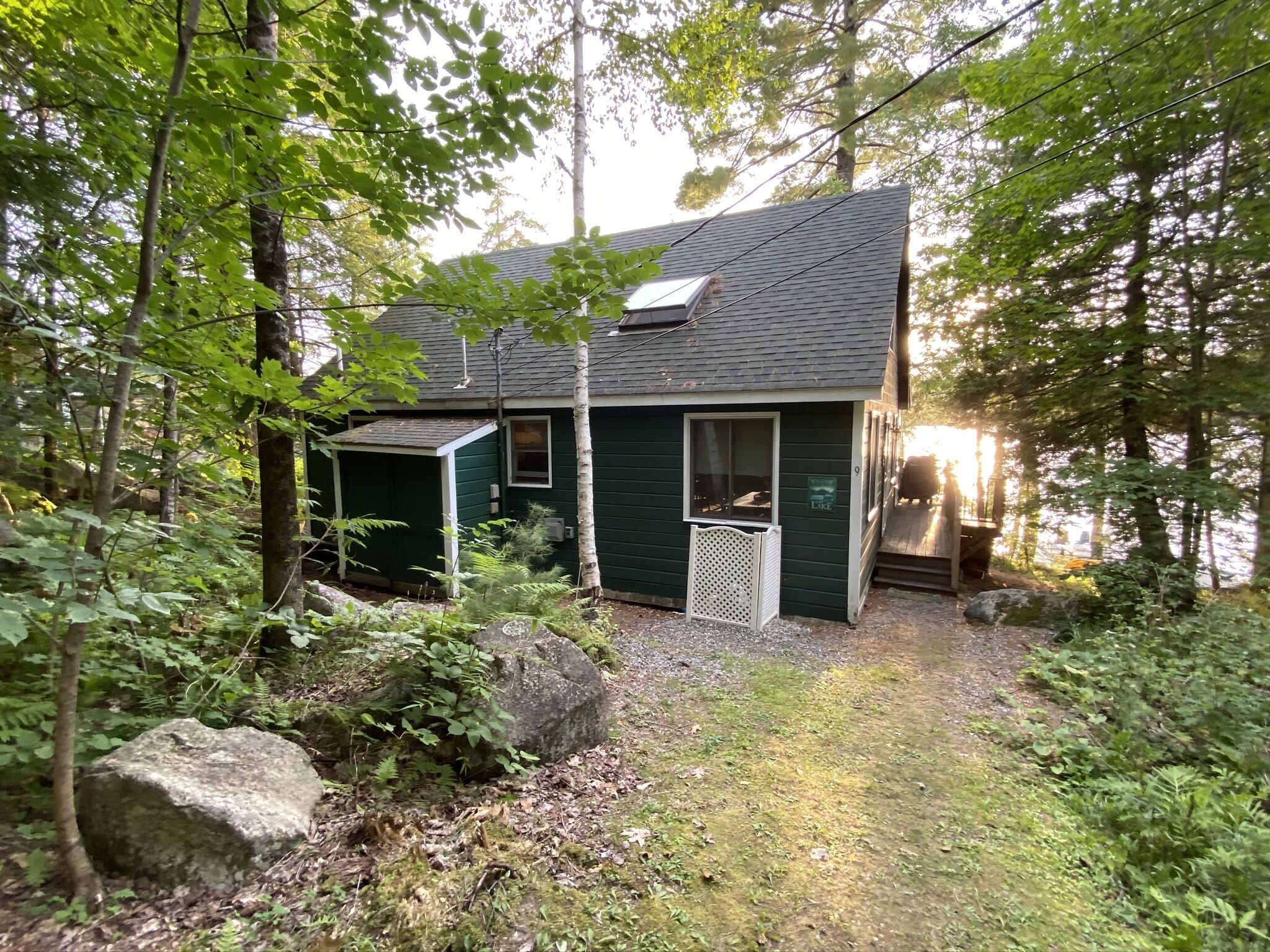 A cabin with a small porch and a covered outdoor area, surrounded by trees and a rocky path.