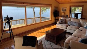A cozy living room with a large window overlooking a lake, a telescope on a tripod, and a comfortable sofa. - Lake house with million dollar view & hot tub (Perryville)